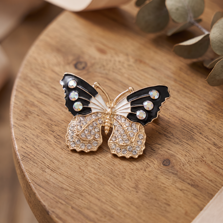 Black and white enamel butterfly brooch pin with iridescent AB crystals and clear pavé lower wings on a white background by Delemon