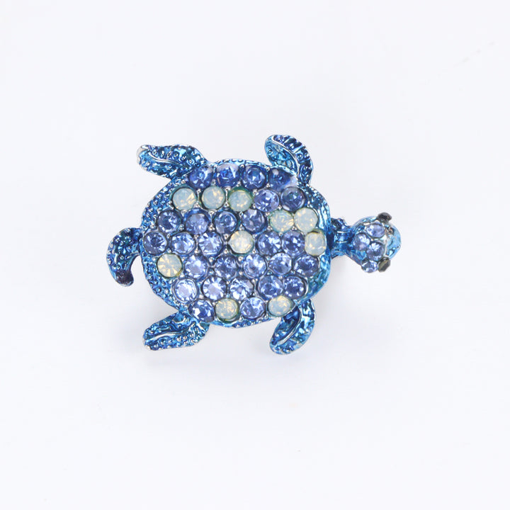 Metallic blue sea turtle brooch pin encrusted with sapphire blue and opal-tone crystals on a white background by Delemon