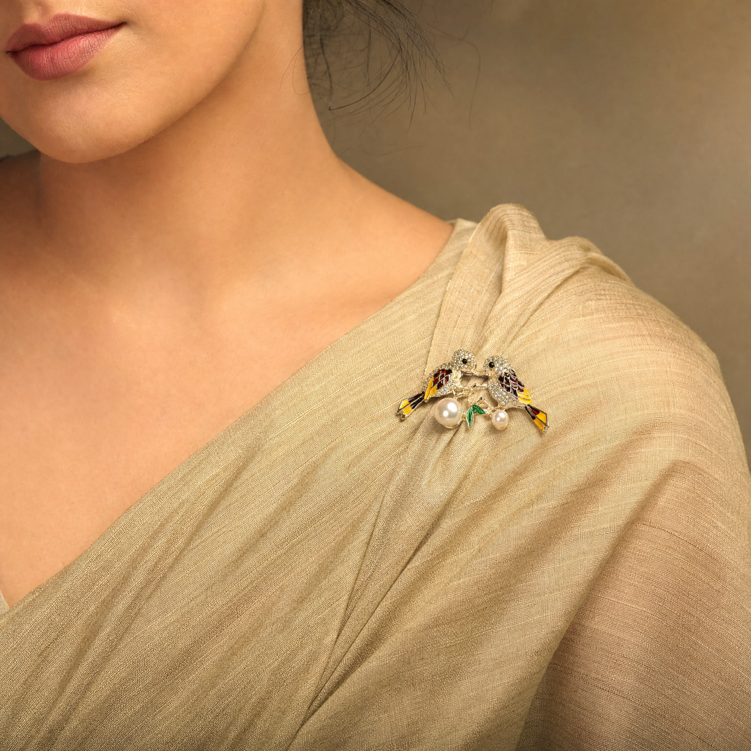 Gold-tone lovebirds brooch pin with clear crystal paved heads, maroon and yellow enamel wings, green leaves, and hanging pearls