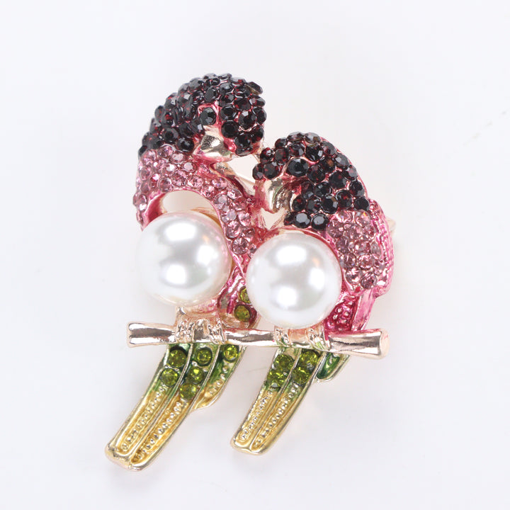 Gold-tone perched lovebirds brooch pin with pink and dark red crystals, olive green tail feathers, and pearl bodies on a white background by Delemon
