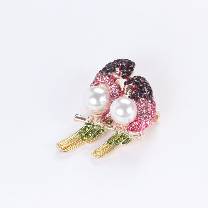 Gold-tone perched lovebirds brooch pin with pink and dark red crystals, olive green tail feathers, and pearl bodies on a white background by Delemon