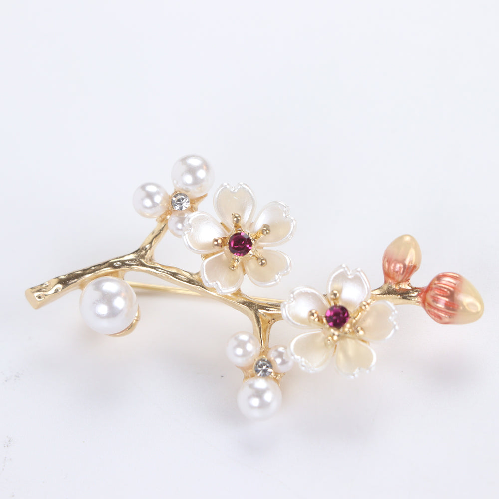 Gold-tone cherry blossom branch brooch pin with pearlescent white enamel flowers, ruby pink crystals, and pearl clusters on a white background by Delemon