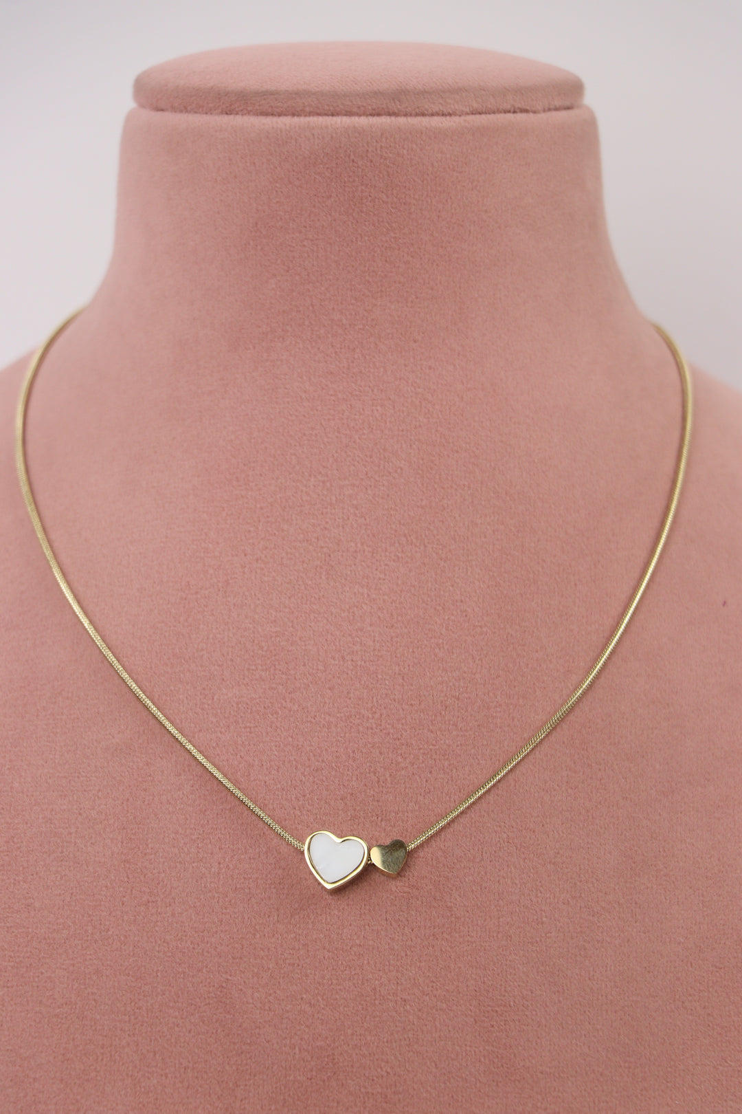 Delemon high-quality gold plated snake chain necklace with double heart charms displayed elegantly on a pink bust.