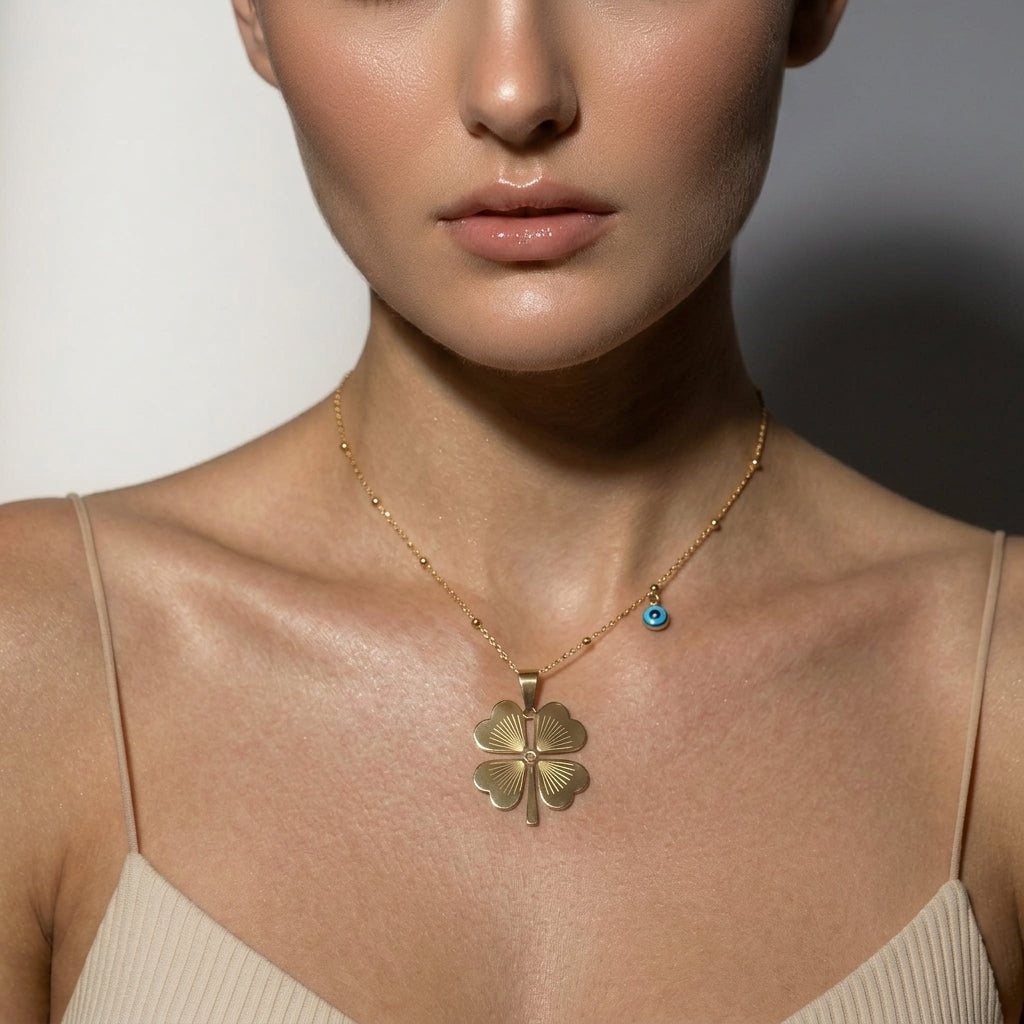 Delemon high-quality gold plated delicate bead chain necklace featuring a large central four-leaf clover pendant with an engraved pattern and a small hanging blue evil eye charm