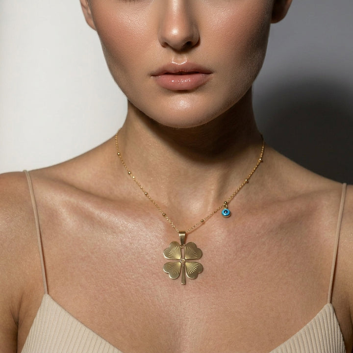 Delemon high-quality gold plated delicate bead chain necklace featuring a large central four-leaf clover pendant with an engraved pattern and a small hanging blue evil eye charm