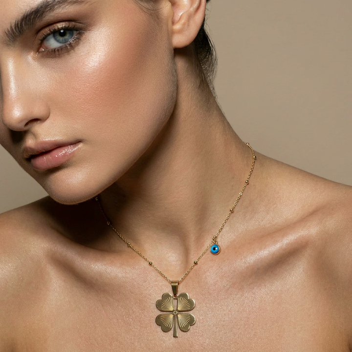 Delemon high-quality gold plated delicate bead chain necklace featuring a large central four-leaf clover pendant with an engraved pattern and a small hanging blue evil eye charm