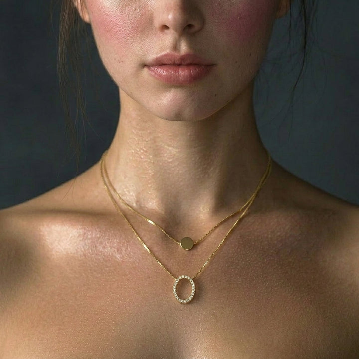 Delemon high-quality gold plated double-layer necklace featuring a top delicate chain with a smooth round disc and a bottom chain with a crystal pave oval ring pendant