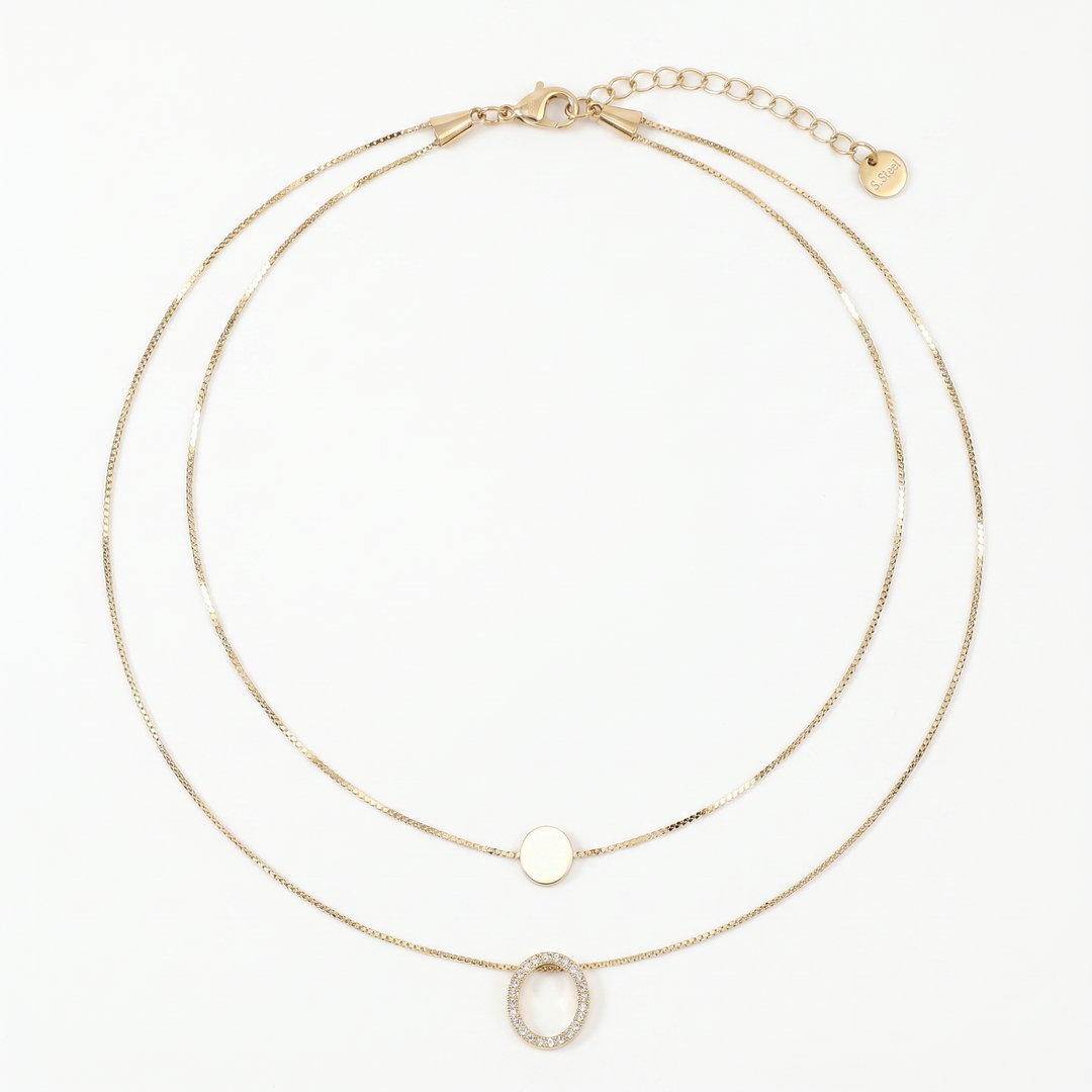 Delemon high-quality gold plated double-layer necklace featuring a top delicate chain with a smooth round disc and a bottom chain with a crystal pave oval ring pendant