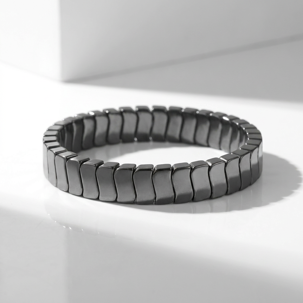 Delemon featuring a uniform stretch bracelet with slim, gently curved polished metallic hematite rectangular drum blocks
