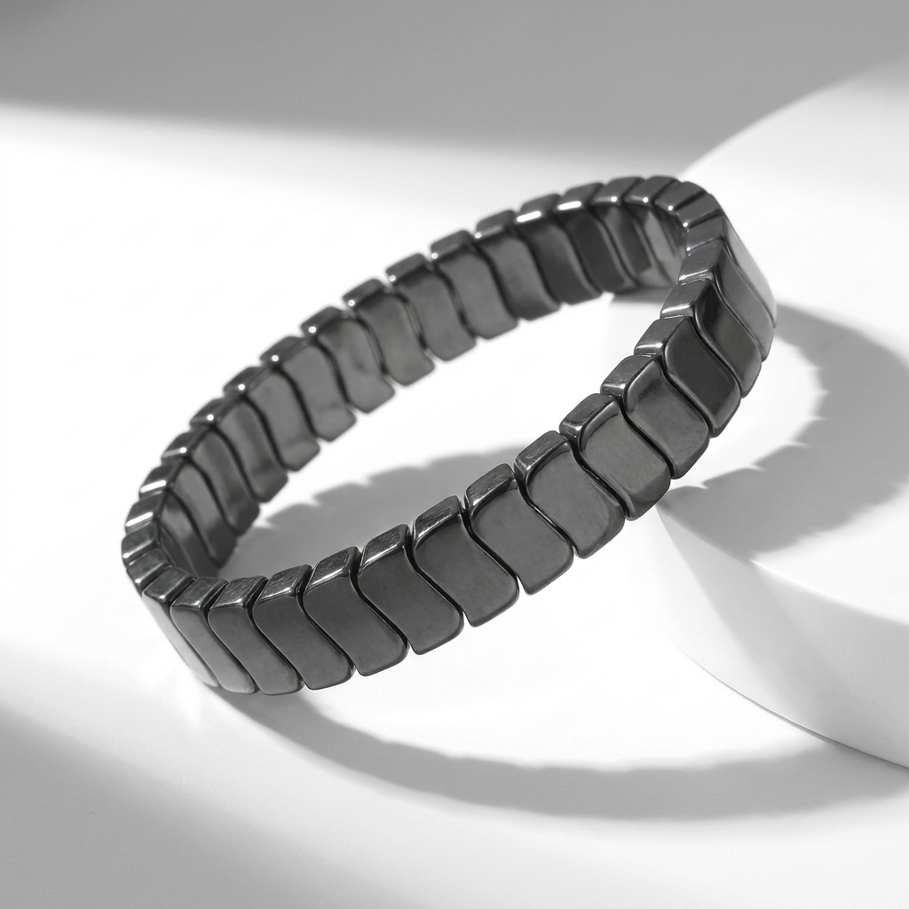Delemon featuring a uniform stretch bracelet with slim, gently curved polished metallic hematite rectangular drum blocks