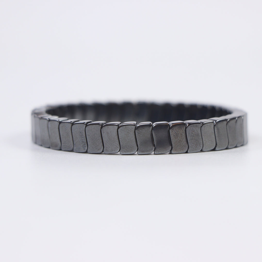 Delemon featuring a uniform stretch bracelet with slim, gently curved polished metallic hematite rectangular drum blocks