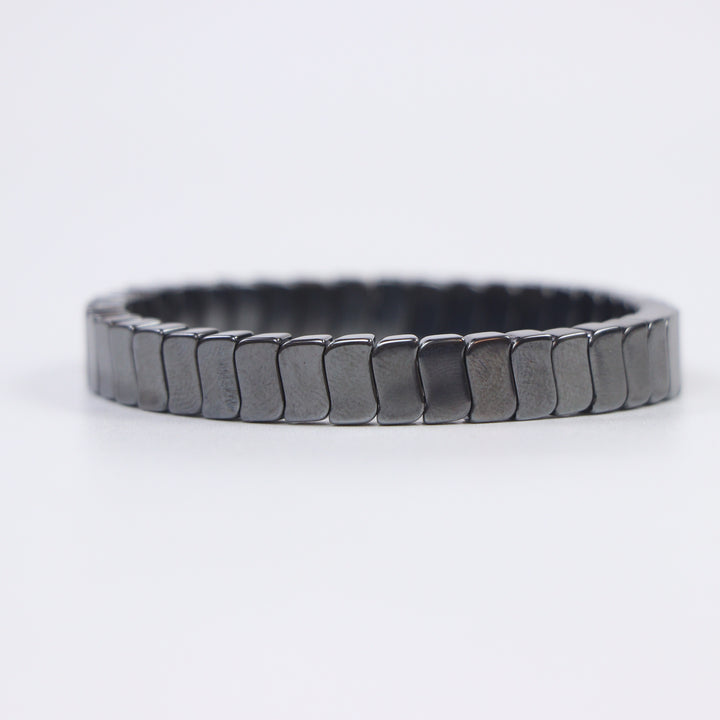 Delemon featuring a uniform stretch bracelet with slim, gently curved polished metallic hematite rectangular drum blocks