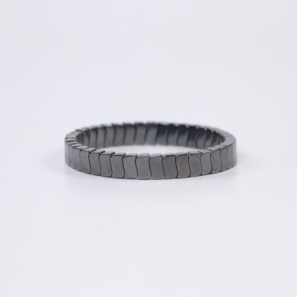 Delemon featuring a uniform stretch bracelet with slim, gently curved polished metallic hematite rectangular drum blocks