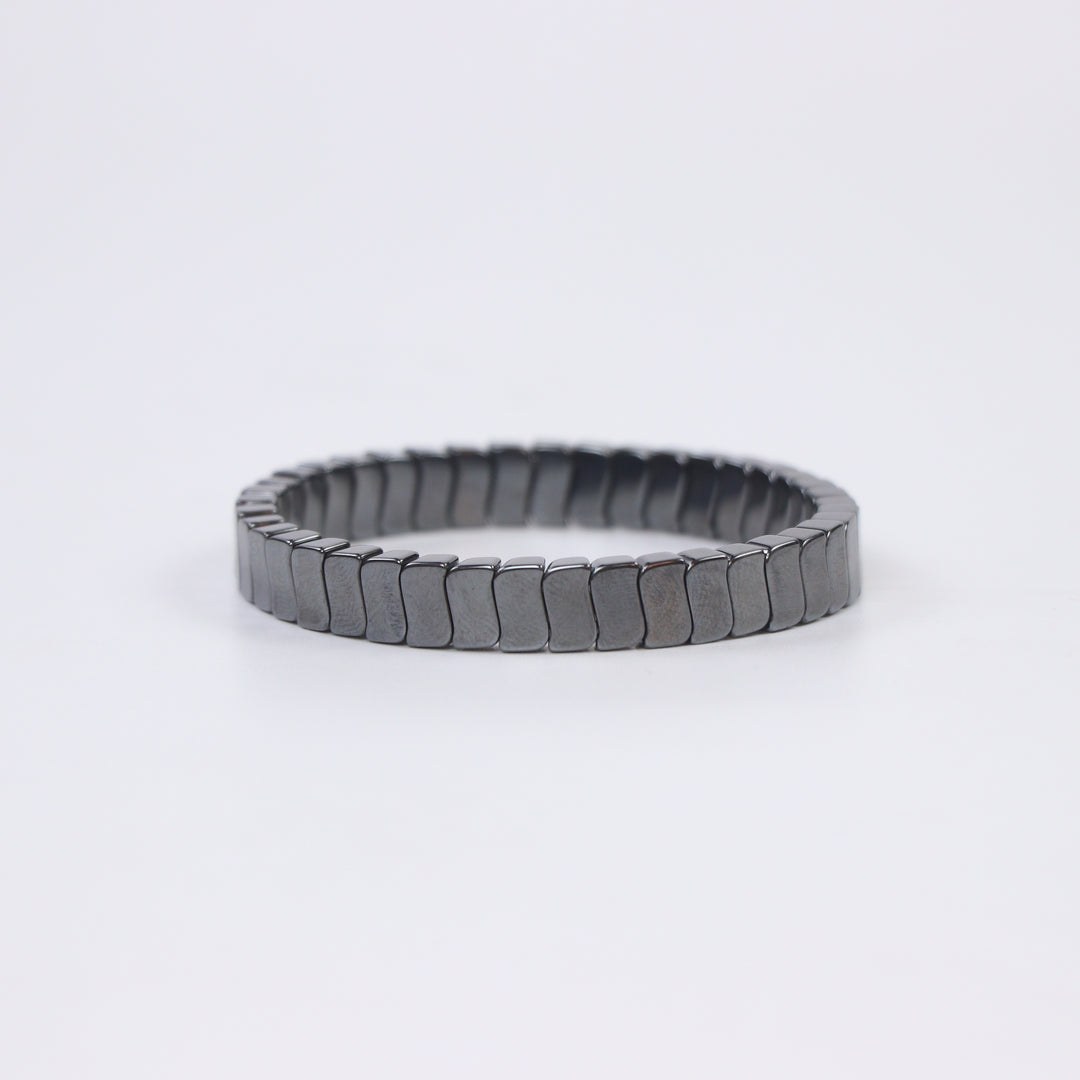 Delemon featuring a uniform stretch bracelet with slim, gently curved polished metallic hematite rectangular drum blocks