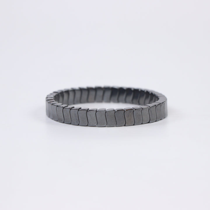 Delemon featuring a uniform stretch bracelet with slim, gently curved polished metallic hematite rectangular drum blocks