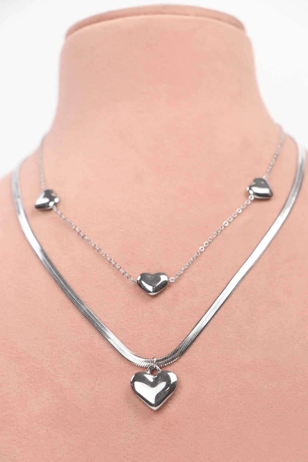 Delemon high-quality silver polished layered necklace featuring a delicate chain with small heart stations and a thick snake chain with a central statement heart pendant front view.