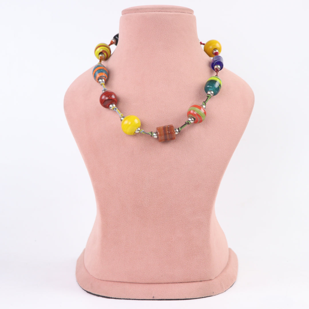 Vibrant hand-painted multicolor glass bead boho necklace on a pink display mannequin - Delemon Collection.