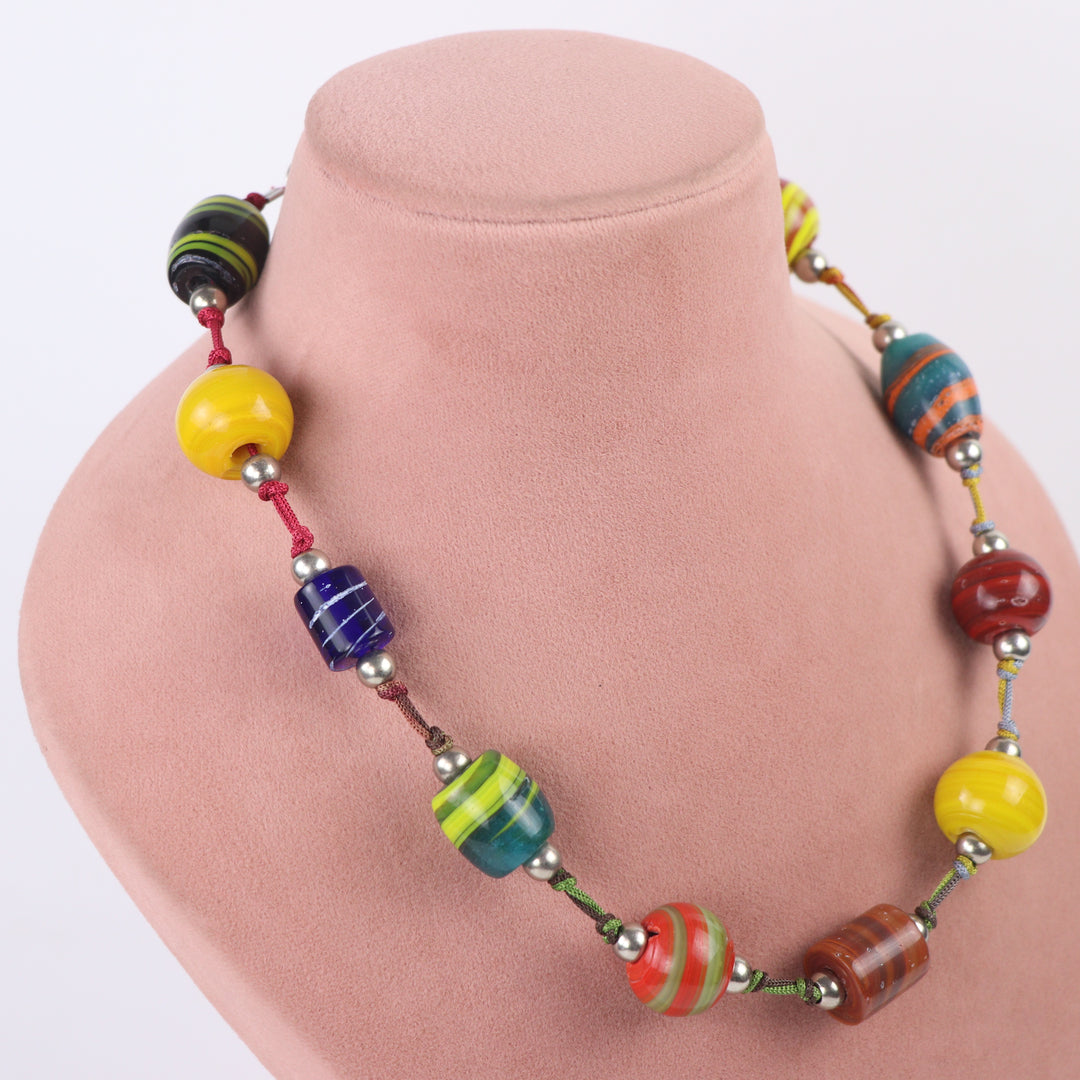 Vibrant hand-painted multicolor glass bead boho necklace on a pink display mannequin - Delemon Collection.
