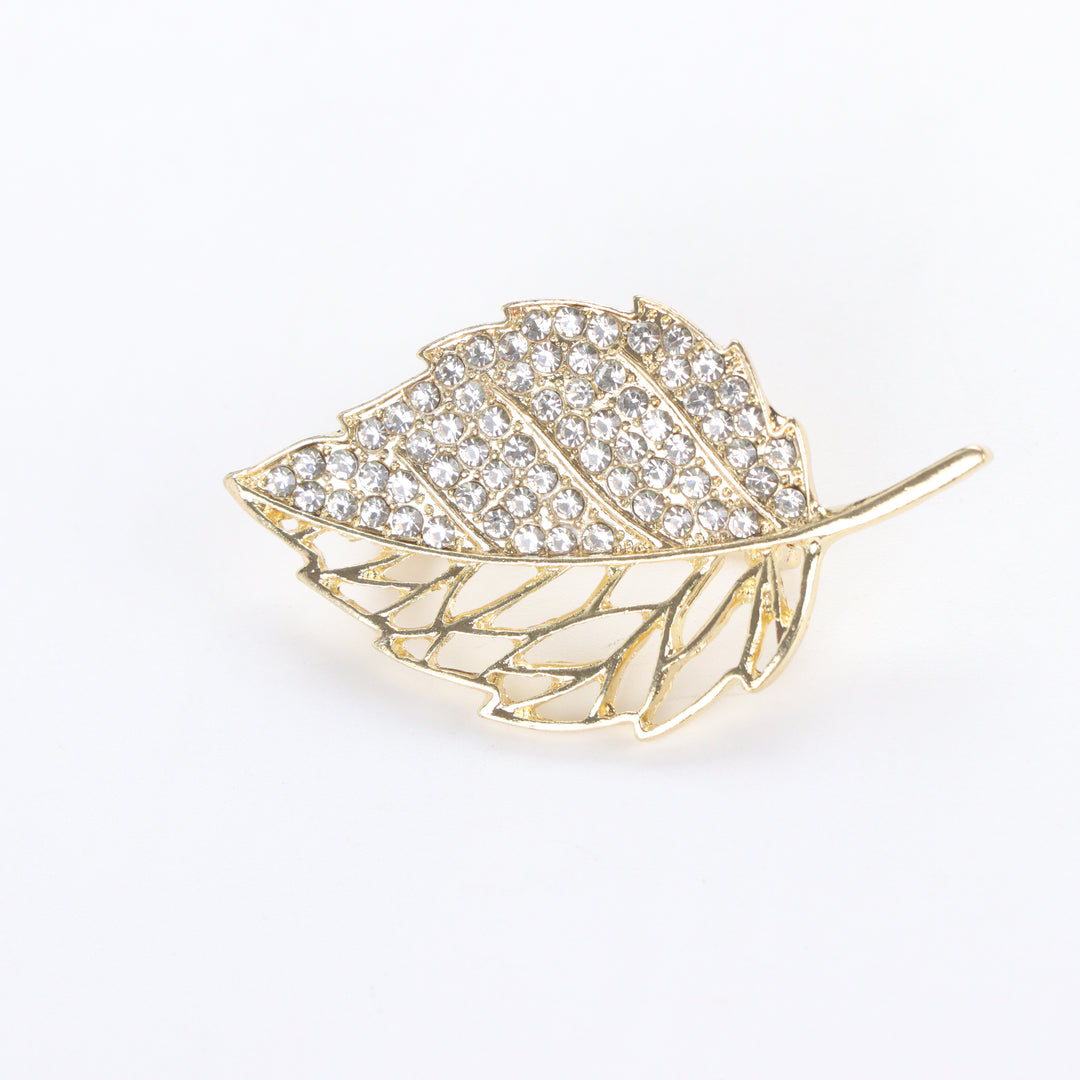 Gold-tone leaf brooch pin with half pave crystal rhinestones and half hollow filigree design on a white background by Delemon