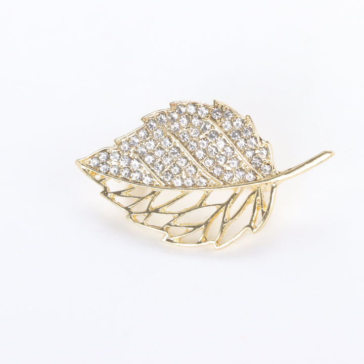 Gold-tone leaf brooch pin with half pave crystal rhinestones and half hollow filigree design on a white background by Delemon