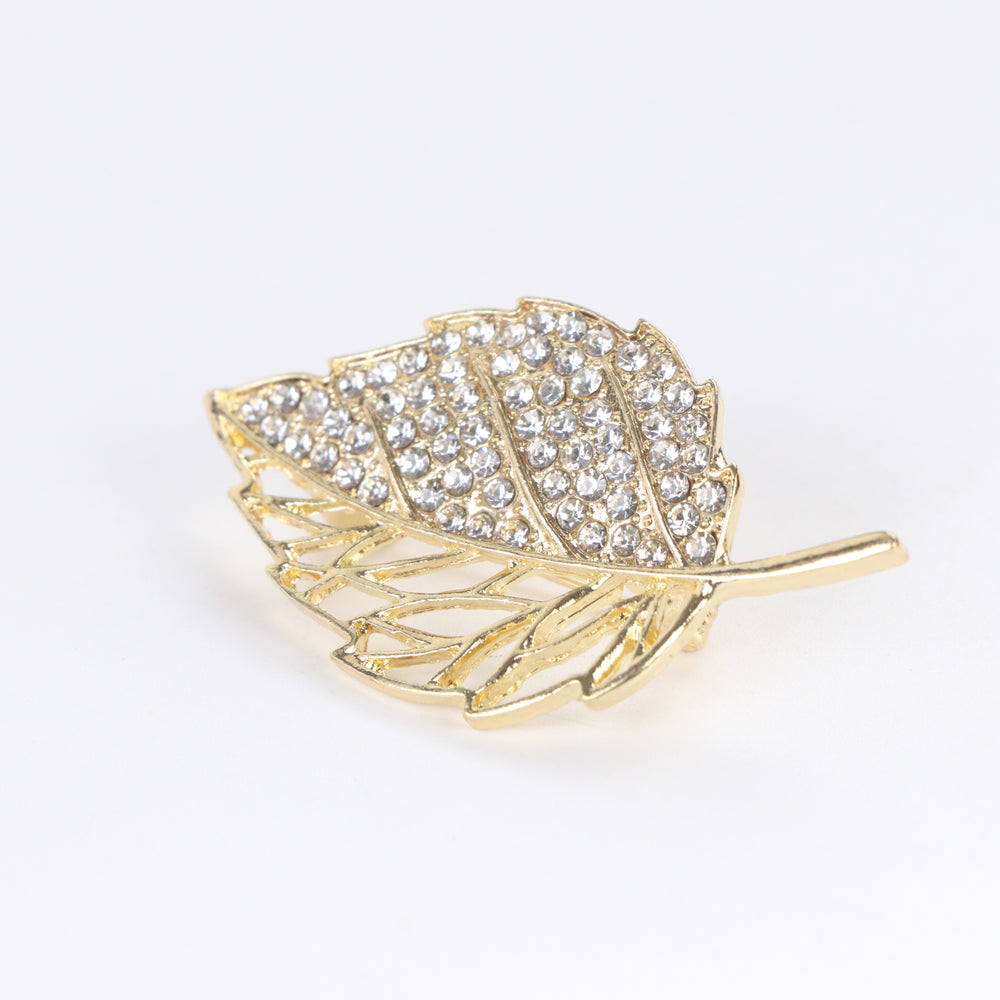 Gold-tone leaf brooch pin with half pave crystal rhinestones and half hollow filigree design on a white background by Delemon