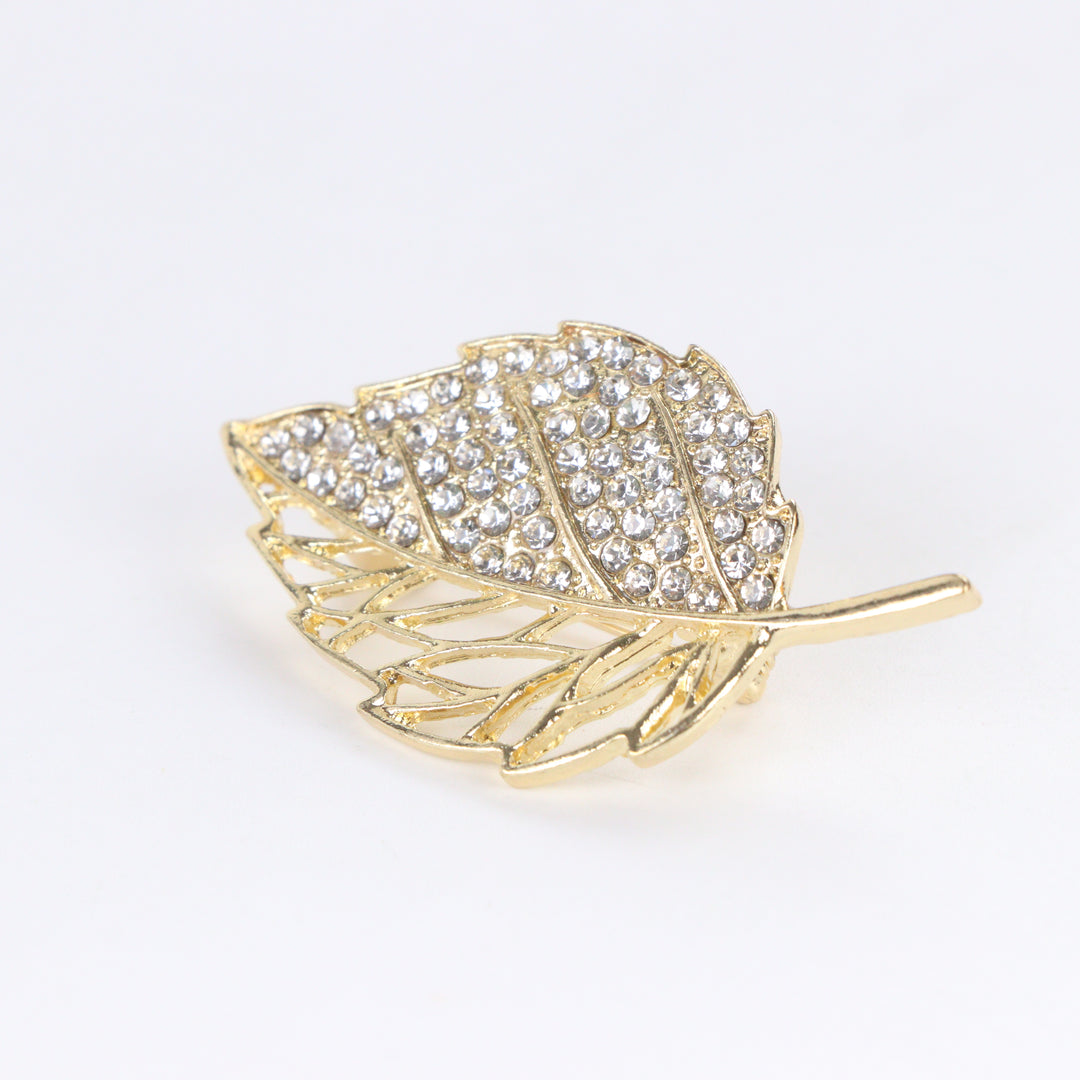 Gold-tone leaf brooch pin with half pave crystal rhinestones and half hollow filigree design on a white background by Delemon
