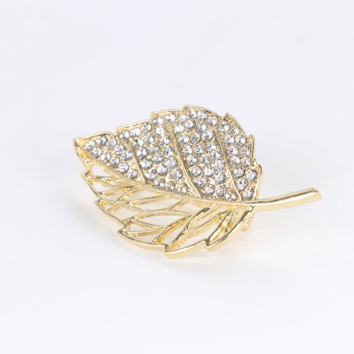 Gold-tone leaf brooch pin with half pave crystal rhinestones and half hollow filigree design on a white background by Delemon