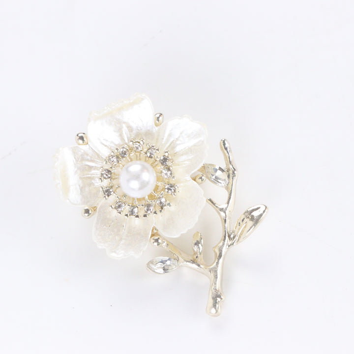 Gold-tone white enamel flower brooch pin with center pearl, rhinestone halo, and crystal branch accents on a white background by Delemon