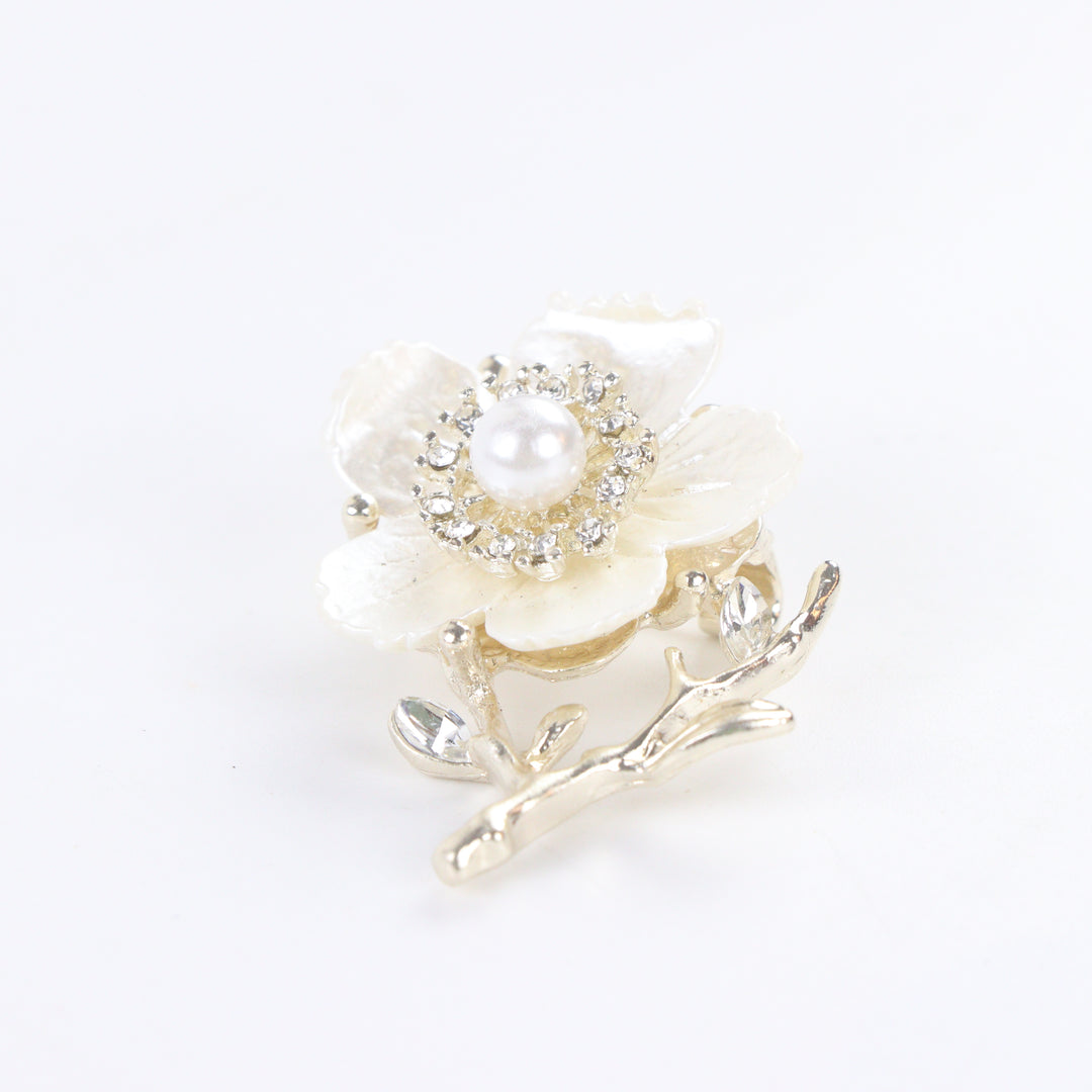 Gold-tone white enamel flower brooch pin with center pearl, rhinestone halo, and crystal branch accents on a white background by Delemon