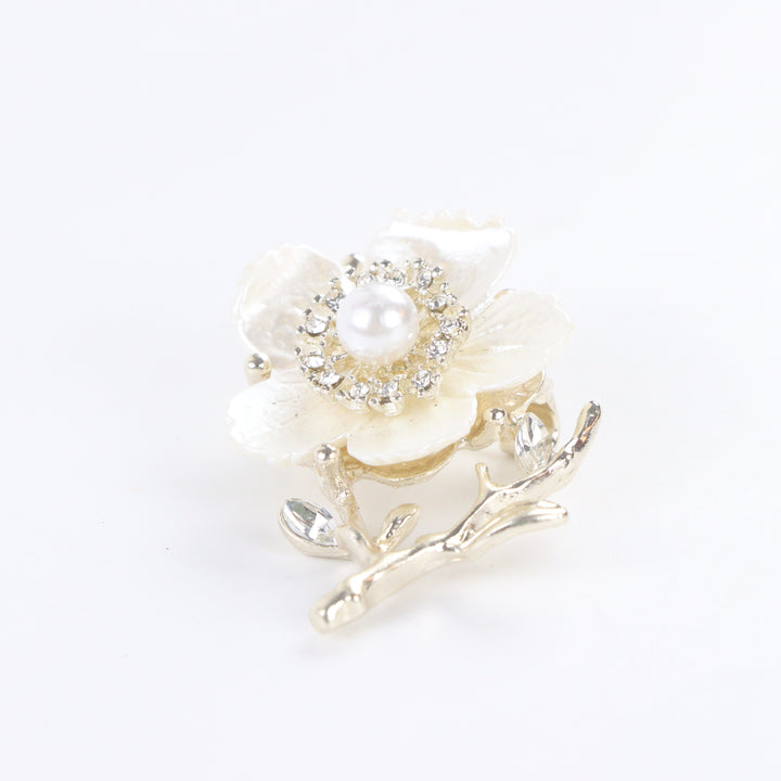 Gold-tone white enamel flower brooch pin with center pearl, rhinestone halo, and crystal branch accents on a white background by Delemon