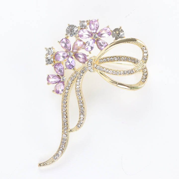 Gold-tone floral bow brooch pin featuring purple tear-drop crystal blossoms and clear pavé rhinestone ribbons on a white background by Delemon