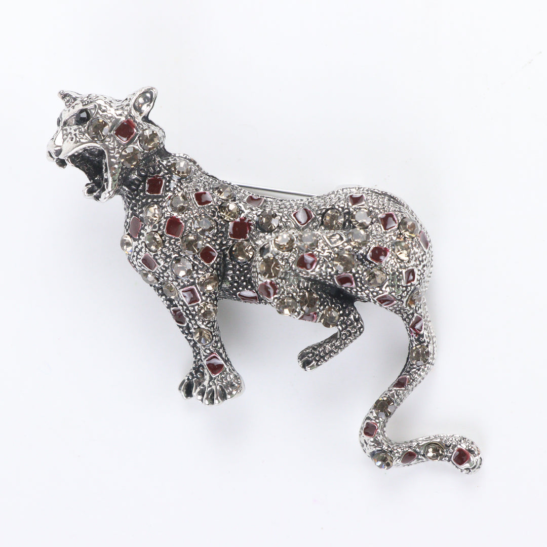 Antique silver-tone stalking leopard brooch pin encrusted with smoky crystals and red enamel leopard spots on a white background by Delemon