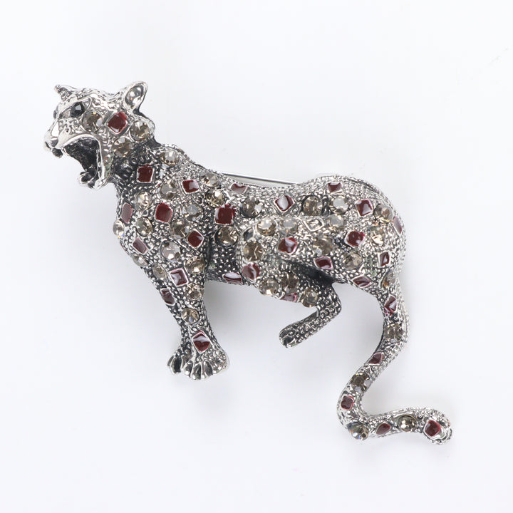 Antique silver-tone stalking leopard brooch pin encrusted with smoky crystals and red enamel leopard spots on a white background by Delemon