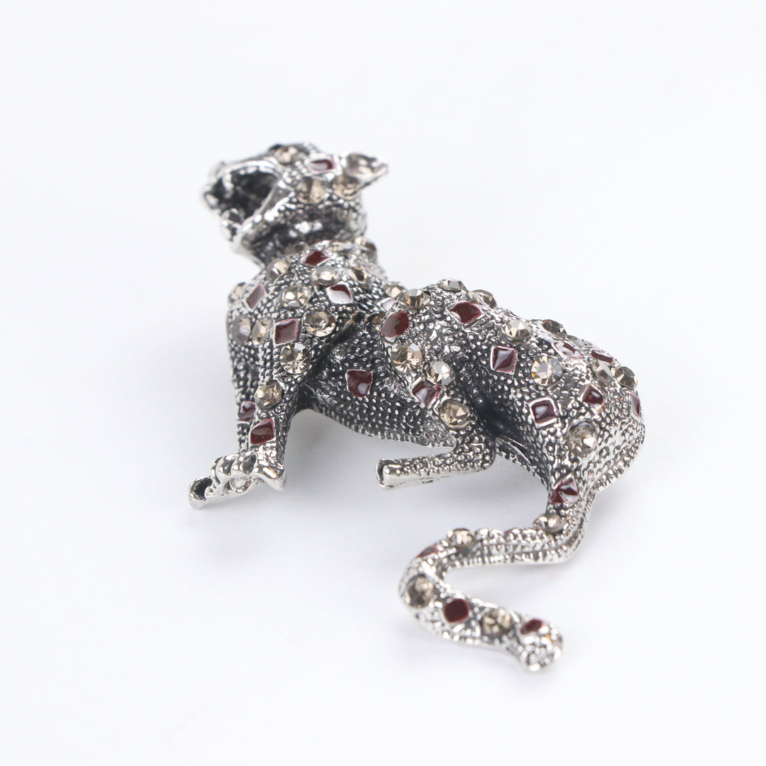Antique silver-tone stalking leopard brooch pin encrusted with smoky crystals and red enamel leopard spots on a white background by Delemon