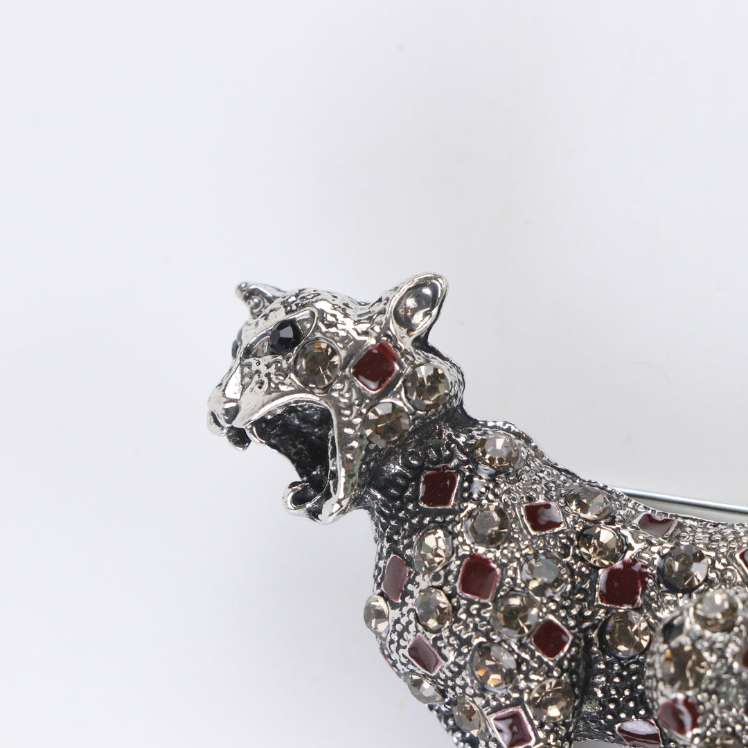 Antique silver-tone stalking leopard brooch pin encrusted with smoky crystals and red enamel leopard spots on a white background by Delemon