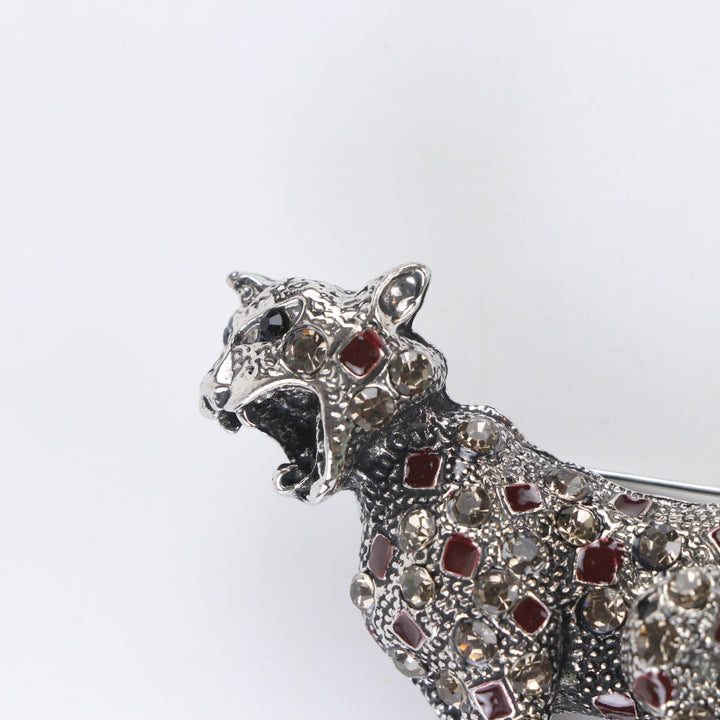 Antique silver-tone stalking leopard brooch pin encrusted with smoky crystals and red enamel leopard spots on a white background by Delemon