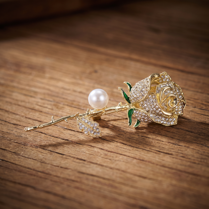 Gold rose brooch pin encrusted with pave crystals, green enamel accents, and a pearl 