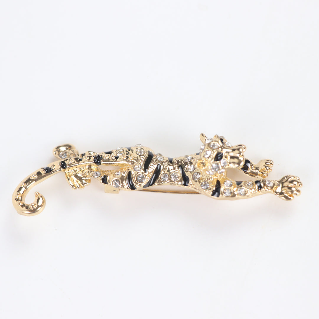 Gold prowling tiger brooch pin encrusted with clear pavé crystals and black enamel stripes on a white background by Delemon
