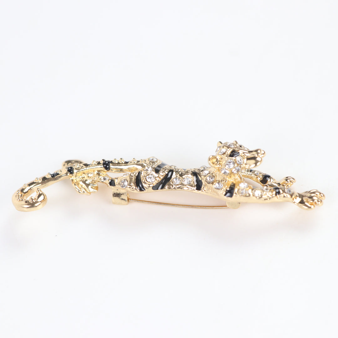 Gold prowling tiger brooch pin encrusted with clear pavé crystals and black enamel stripes on a white background by Delemon