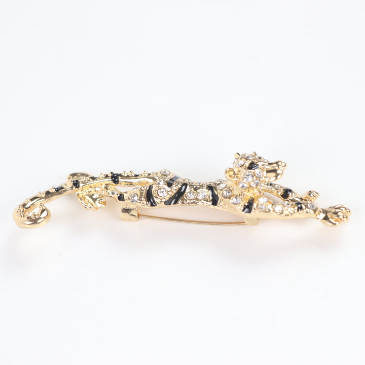 Gold prowling tiger brooch pin encrusted with clear pavé crystals and black enamel stripes on a white background by Delemon