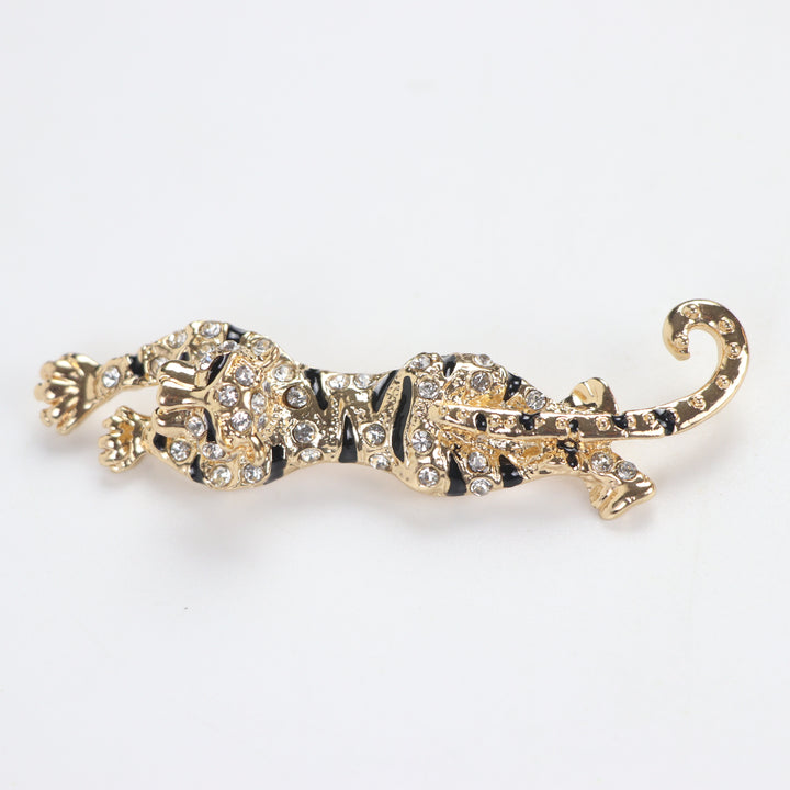 Gold prowling tiger brooch pin encrusted with clear pavé crystals and black enamel stripes on a white background by Delemon