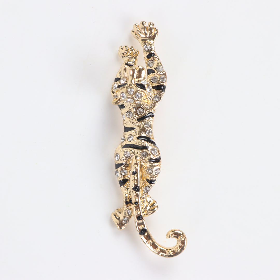 Gold prowling tiger brooch pin encrusted with clear pavé crystals and black enamel stripes on a white background by Delemon