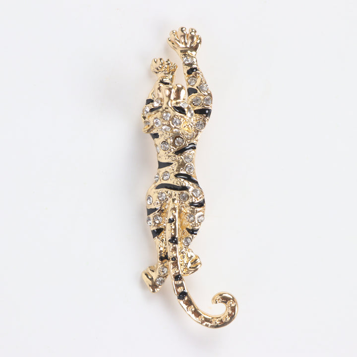 Gold prowling tiger brooch pin encrusted with clear pavé crystals and black enamel stripes on a white background by Delemon