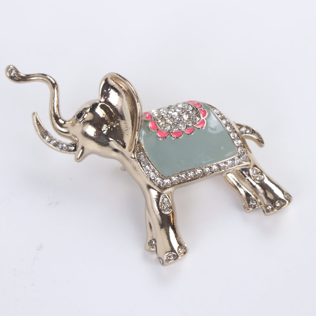 Polished gold-tone trunk-up elephant brooch pin with sage green enamel and clear crystal saddle on a white background by Delemon