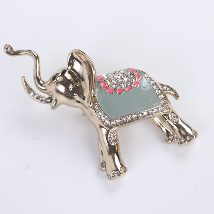 Polished gold-tone trunk-up elephant brooch pin with sage green enamel and clear crystal saddle on a white background by Delemon