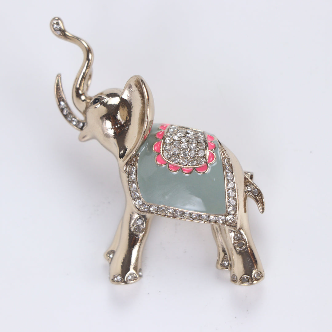 Polished gold-tone trunk-up elephant brooch pin with sage green enamel and clear crystal saddle on a white background by Delemon
