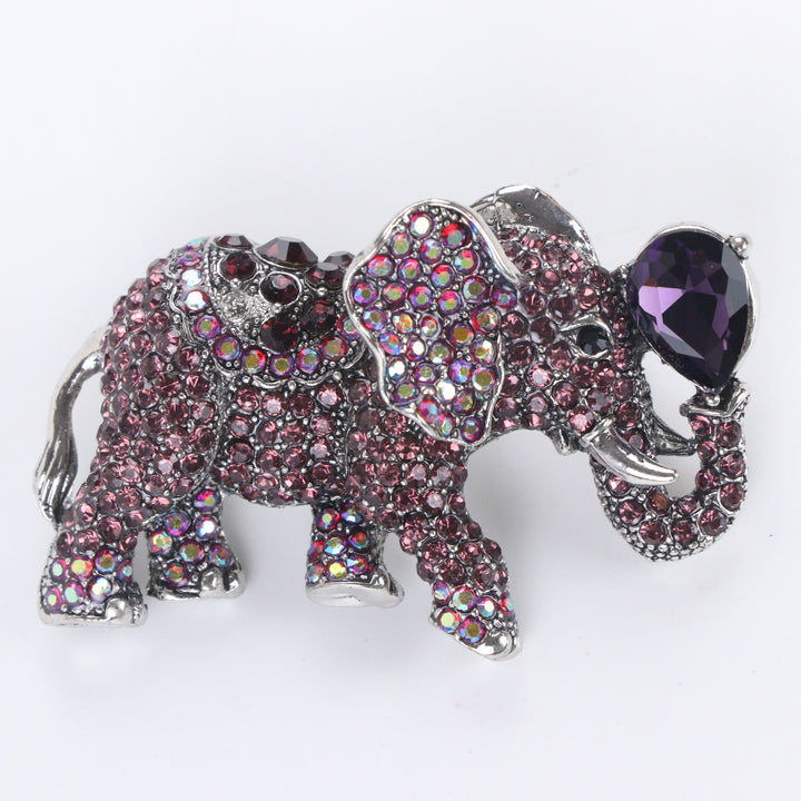 Antique silver-tone elephant brooch pin pavé-set with purple and iridescent crystals holding a pear-cut purple jewel in its raised trunk on a white background by Delemon