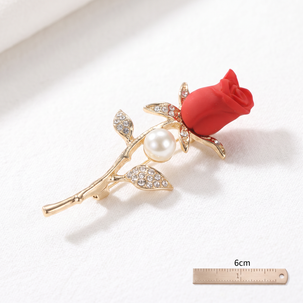 Matte red rose flower brooch pin with a pearl accent and pave crystal leaves on a gold stem against a white background by Delemon