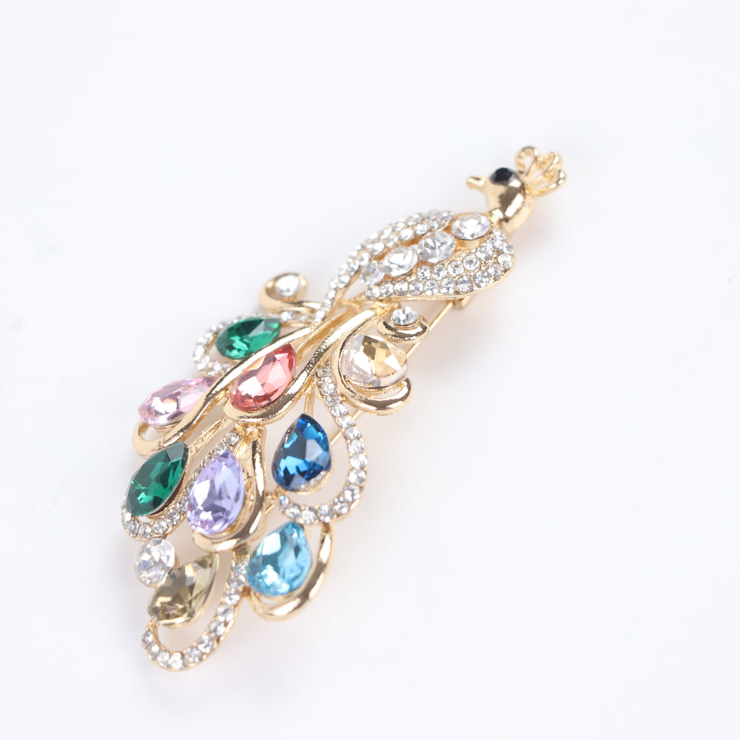 Sparkling gold peacock brooch pin adorned with colorful teardrop-cut crystals and clear pavé rhinestones against a white background by Delemon
