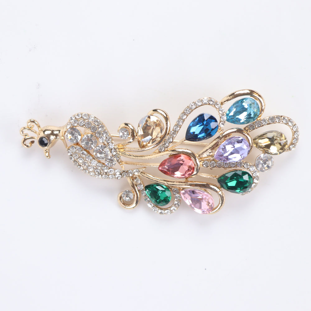 Sparkling gold peacock brooch pin adorned with colorful teardrop-cut crystals and clear pavé rhinestones against a white background by Delemon